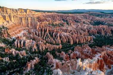 Birçok kırmızı kaya oluşumuna sahip bir kanyonun panoramik görüntüsü. Gökyüzü turuncu ve mavi renklerin karışımıdır.