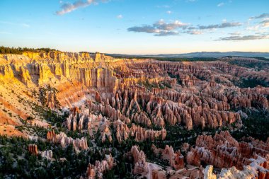 Bir sürü kırmızı kayanın olduğu güzel bir kanyon manzarası. Gökyüzü mavi ve güneş batıyor.