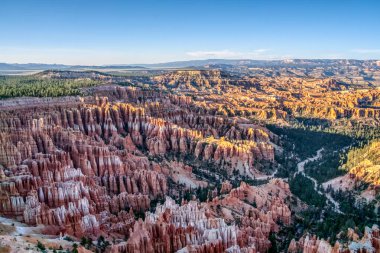 Arkasında büyük bir kanyon ve dağlar olan güzel bir manzara. Kanyon kırmızı ve beyaz kayalarla dolu, görkemli ve hayranlık uyandırıcı bir görüntü veriyor. Gökyüzü açık.