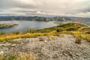 Uzakta gölü olan bir dağın tepesi. Gökyüzü bulutlu ve manzara sakin.