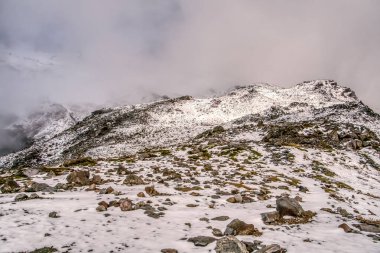 Arkasında bulutlu bir gökyüzü olan karlı bir dağ. Kar zemini ve kayaları kaplıyor.