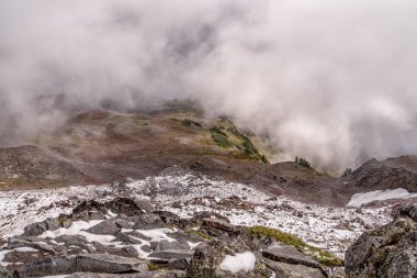 Kar ve bulutlarla kaplı bir dağ. Gökyüzü bulutlu ve dağ karla kaplı.