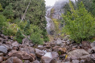 Arka planda şelale olan kayalık bir dere. Su berrak ve kayalar büyük.