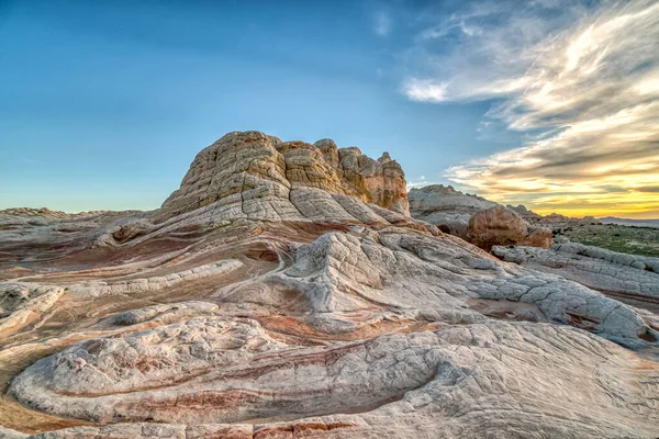 Kayalık, çorak bir arazi. Önünde büyük, beyaz bir kaya var. Gökyüzü mavi ve güneş batıyor. Huzurlu ve huzurlu bir atmosfer yaratıyor.