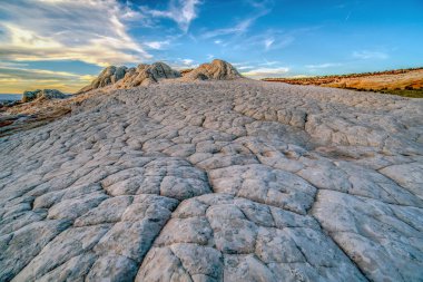 Gökyüzünde birkaç bulut olan kayalık, çorak bir arazi. Gökyüzü mavi ve güneş batıyor.