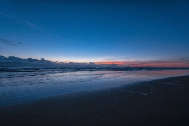 Mavi gökyüzü ve pembe ve turuncu gün batımlı güzel bir plaj sahnesi. Su sakin ve gökyüzü berrak.