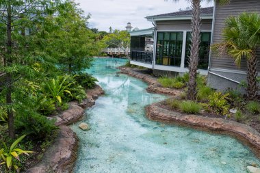 Küçük bir su akıntısı yemyeşil bir alanda akar. Su berrak ve sakin, ve çevresi ağaçlar ve bitkilerle dolu. Huzurlu ve huzurlu bir sahne.