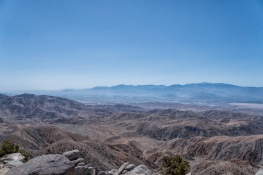 Gökyüzü açık ve mavidir ve dağlar uzaktadır. Manzara kuru ve çorak, görünürde ağaç ya da bitki yok.