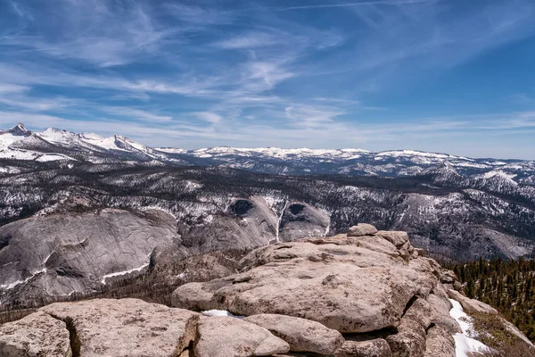 Arkasında açık mavi gökyüzü olan karla kaplı bir dağ sırası. Dağlar kalın bir kar tabakasıyla kaplı, onlara heybetli ve huzurlu bir görünüm veriyor.