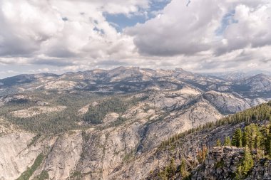 Dağ sırası yemyeşil ağaçlarla kaplıdır ve gökyüzü bulutlarla kaplıdır. Sahne sakin ve sakin, dağlar manzara için güzel bir zemin sağlıyor.