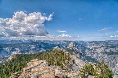 Açık mavi gökyüzü ve bulutları olan bir dağ sırası. Bulutlar gökyüzüne dağıldı ve dağlar uzaklardan görülebiliyor.