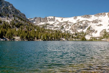 Dağlarla çevrili güzel bir göl. Su sakin ve berrak, yukarıdaki mavi gökyüzünü yansıtıyor. Huzurlu ve huzurlu bir sahne.