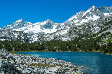 Önünde göl olan güzel bir dağ sırası. Göl sakin ve berrak, yukarıdaki mavi gökyüzünü yansıtıyor. Dağlar karla kaplı. Huzurlu ve huzurlu bir atmosfer yaratıyorlar.
