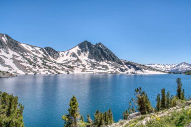 Önünde büyük bir su kütlesi olan güzel bir dağ sırası. Gökyüzü berrak ve mavi, su sakin ve durgun. Sahne huzurlu ve sakin, dağlarla birlikte.