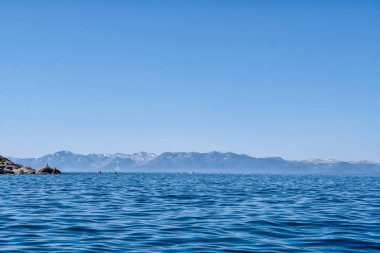 Arkasında dağlar olan güzel mavi bir okyanus. Gökyüzü açık ve güneş parlıyor.