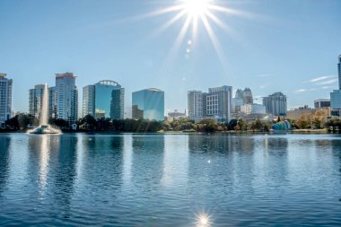 Arka planda büyük bir su kütlesi olan bir şehir silueti. Su sakin ve uzaktaki binaları yansıtıyor.
