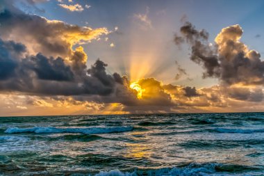 Güneş okyanusun üzerinde batıyor, suyun üzerine sıcak bir parıltı saçıyor. Gökyüzü bulutlarla dolu, karamsar bir atmosfer yaratıyor.
