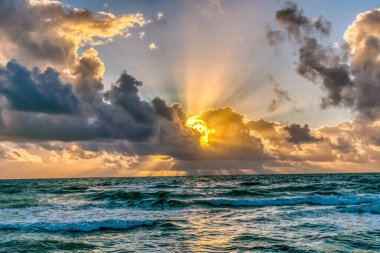 Güneş okyanusun üzerindeki bulutların arasından parlıyor. Gökyüzü mavi ve beyaz bulutların karışımıdır.