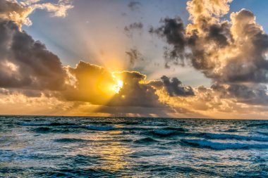 Güneş okyanusun üzerinde batıyor, suyun üzerine sıcak bir parıltı saçıyor. Gökyüzü bulutlarla dolu, karamsar bir atmosfer yaratıyor.