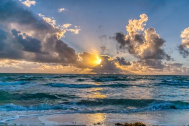 Gökyüzü bulutlu ve güneş batıyor. Okyanus sakin ve su mavi.