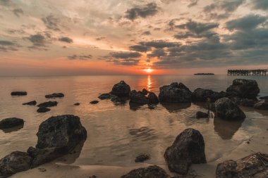 Arka planda büyük bir su kütlesi olan kayalık bir sahil. Güneş batıyor, sahne üzerine sıcak bir parıltı saçıyor.