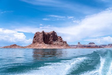 Bir tekne büyük bir kaya oluşumunun yakınında suda ilerliyor. Gökyüzü açık ve mavi, ve su sakin