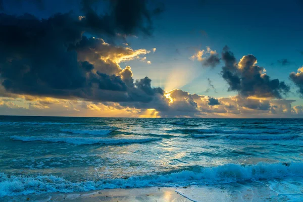 Gökyüzü bulutlu ve güneş okyanusun üzerinde batıyor. Su sakin ve gökyüzü mavi ve turuncu karışımı.