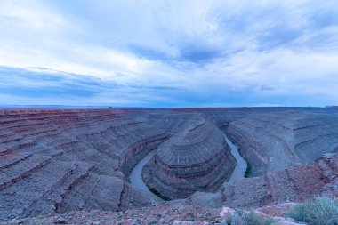 İçinden nehir akan bir kanyon. Gökyüzü bulutlu ve güneş batıyor.