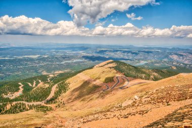 Zirveye çıkan dolambaçlı bir yolu olan bir dağ sırası. Yol ağaçlarla çevrili ve gökyüzü açık.