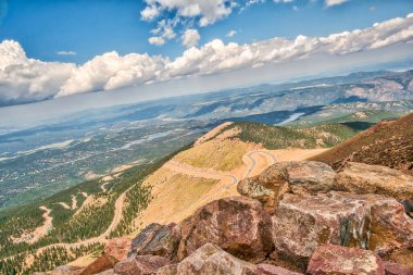 Tepesinde yol olan bir dağ. Yol dönüyor ve arka planda ağaçlar var.