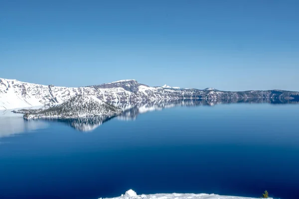 Arkadaki dağlarda kar olan güzel mavi bir göl. Sudaki dağların yansıması huzurlu ve huzurlu bir atmosfer yaratır.