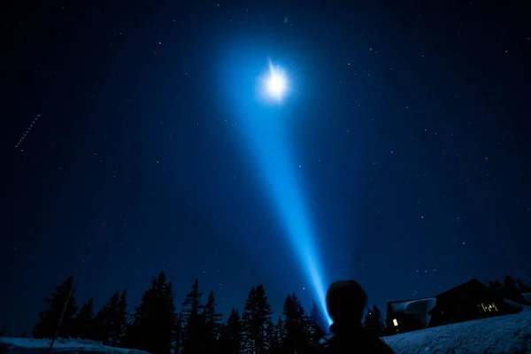 Bir insan elinde bir fenerle karda duruyor, gökyüzüne bakıyor. Gökyüzü yıldızlar ve parlak bir ay ile dolu. Sahnenin huzurlu ve huzurlu bir havası var.