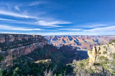 Büyük Kanyon 'un manzarası nefes kesicidir. Arka planda dağlar ve yukarıda gökyüzü vardır.