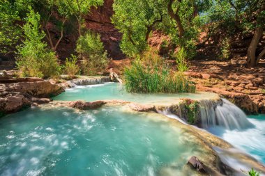 İçinde su akan güzel bir şelale. Su berrak ve mavi, ve çevresi yemyeşil ve yemyeşil. Sahne huzurlu ve huzurlu. Rahatlamak için harika bir yer.