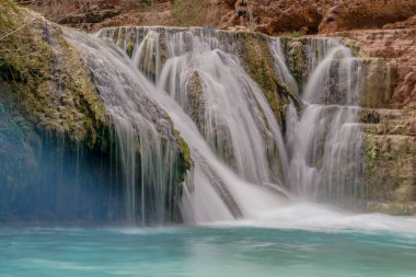 Altında mavi bir nehir akan bir şelale. Su berrak ve sakin. Huzurlu ve huzurlu bir sahne.