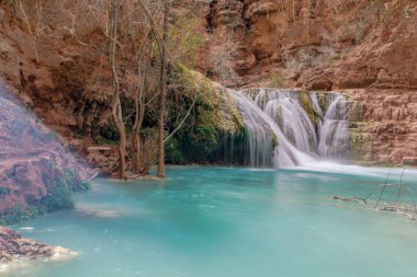 Güzel bir şelale mavi bir nehre akıyor. Su berrak ve sakin. Çevresi yemyeşil ve yemyeşil. Sahne huzurlu ve huzurlu. Rahatlamak için harika bir yer.