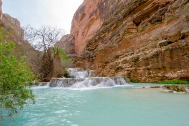 Güzel bir şelale nehre akıyor. Su berrak ve mavidir ve nehri çevreleyen kayalar kahverengidir. Sahne huzurlu ve sakin, suyun sesiyle.