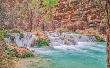 İçinden mavi bir nehir akan güzel bir şelale. Su kristal kadar berrak ve şelaleyi çevreleyen kayalar kahverengi. Huzurlu ve huzurlu bir sahne.