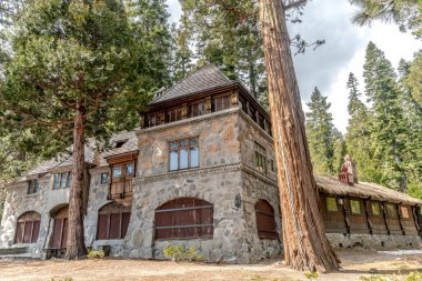 Önünde ağaç olan büyük taştan bir ev. Ev eski ve kırsal bir havası var.