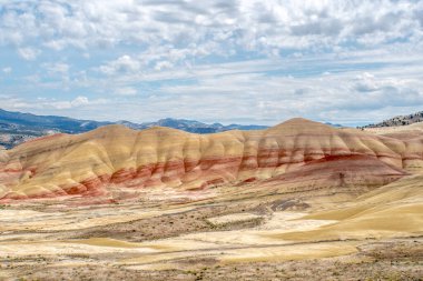 Kırmızı ve sarı desenli bir dağ sırası. Gökyüzü bulutlu ve güneş parlıyor