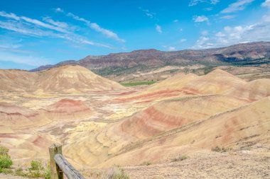 Sarı ve kırmızı dağ sırası olan güzel bir manzara. Gökyüzü açık ve mavi. Dağlar çimlerle kaplı ve toprak kuru ve kayalık.