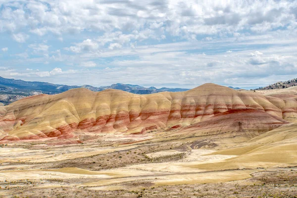 Kırmızı ve sarı desenli bir dağ sırası. Gökyüzü bulutlu ve güneş parlıyor
