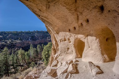 Arka planda mavi gökyüzü olan büyük bir kaya oluşumu. Kaya oluşumunda bir sürü delik var ve görünüşe göre kayadan oyulmuş.