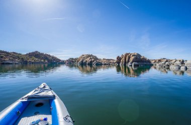 Bir kano, üzerinde açık mavi bir gökyüzü olan bir gölde yüzüyor. Su sakin ve huzurlu. Çevresindeki manzara ise engebeli ve kayalık. Huzur ve macera kavramı