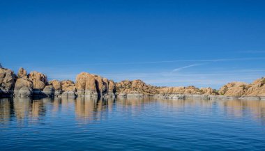 Kayalık bir kıyı şeridi olan güzel mavi bir göl. Su sakin ve durgun, yukarıdaki gökyüzünü yansıtıyor. Huzurlu ve huzurlu bir sahne.