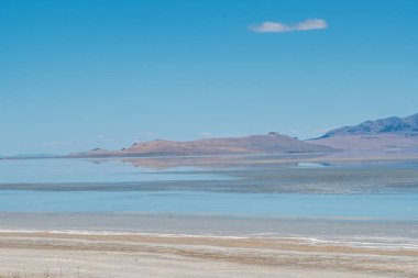 Arkasında dağ olan güzel mavi bir okyanus. Gökyüzü açık ve güneş parlıyor.