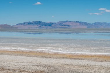 Arka planda dağ sırası olan büyük bir su kütlesi. Gökyüzü açık ve mavi