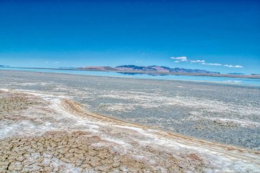 Arkasında mavi gökyüzü olan ıssız bir çöl manzarası. Gökyüzü berrak ve parlak, toprak ise çorak ve kuru.