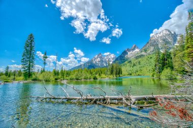 Berrak mavi bir gökyüzü ve sakin bir gölü olan güzel bir dağ sırası. Göl ağaçlarla çevrilidir ve dağlar arka plandadır. Huzurlu ve huzurlu bir sahne.