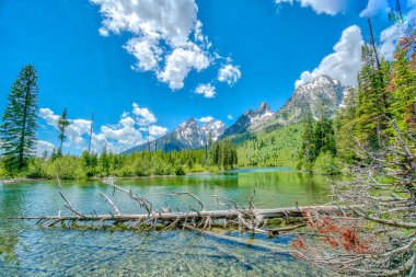 Berrak mavi bir gökyüzü ve sakin bir gölü olan güzel bir dağ sırası. Göl ağaçlarla çevrilidir ve dağlar arka plandadır. Huzurlu ve huzurlu bir sahne.